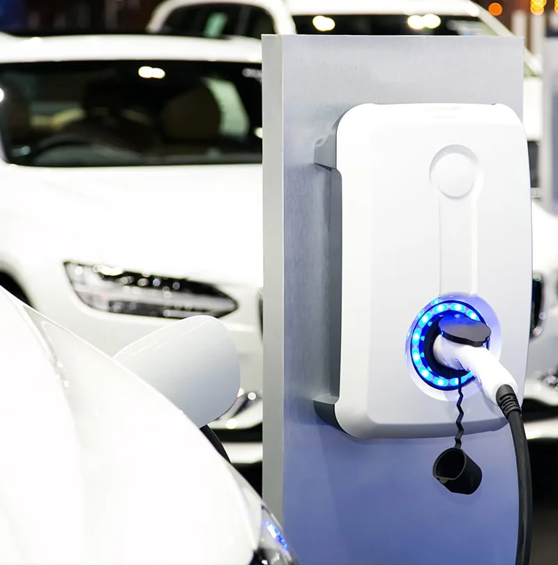 Fotografía de un punto de recarga con el conector enchufado a un coche eléctrico blanco